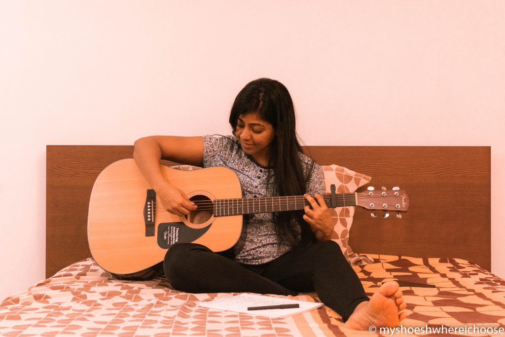 Girl sitting on bed and enjoying a guitar session.