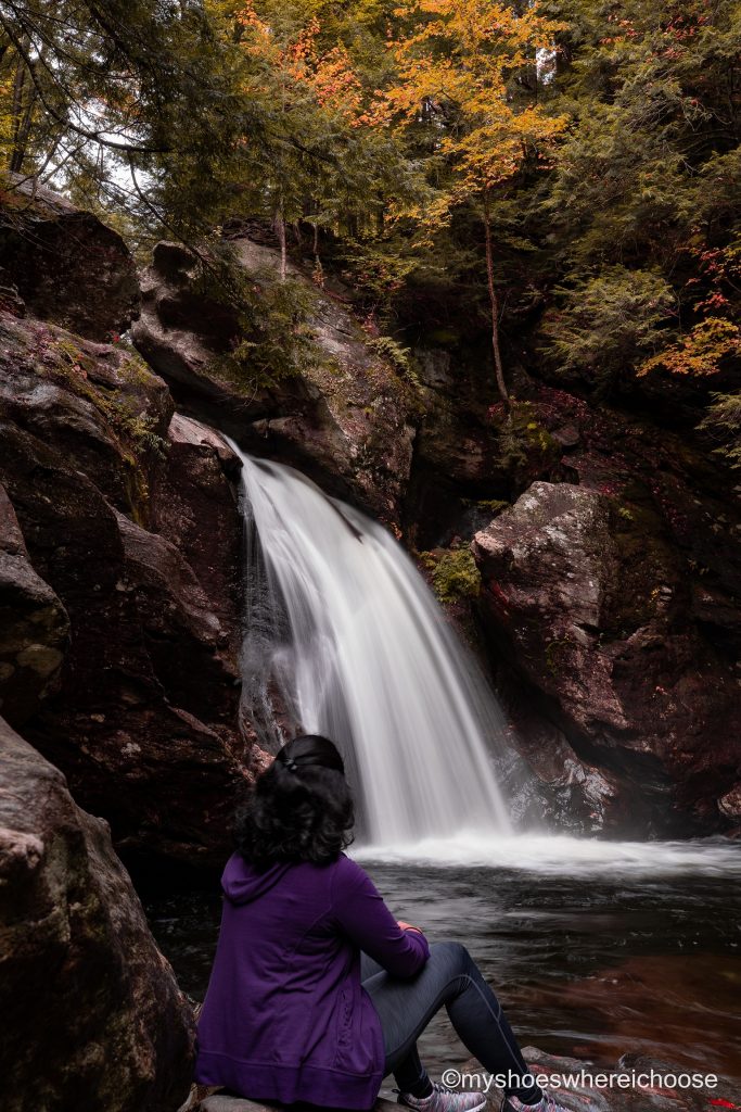 Girl sitting in front of Bingham Falls New England during fall at Stowe Vermont